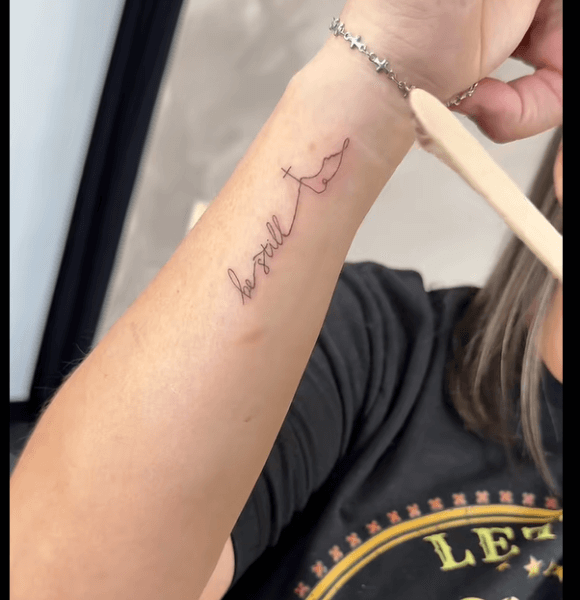 A "Be still." quote tattoo on hand.
